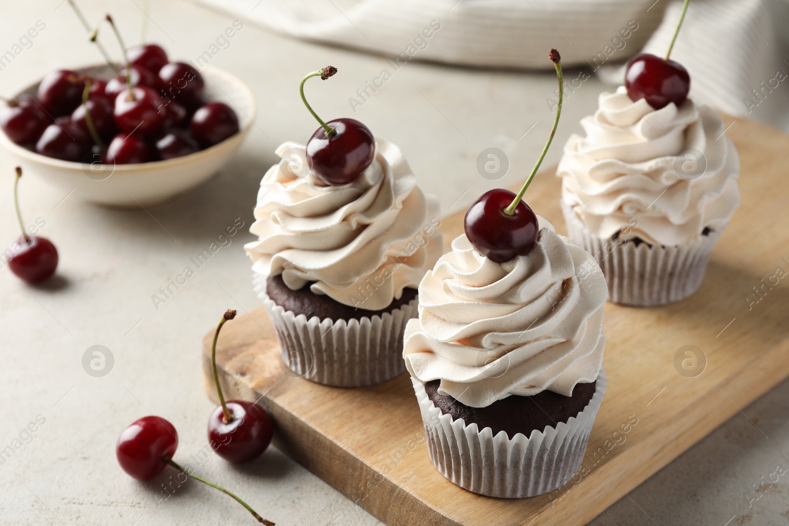 Photo of Delicious cupcakes with cream and cherries on light textured table, closeup