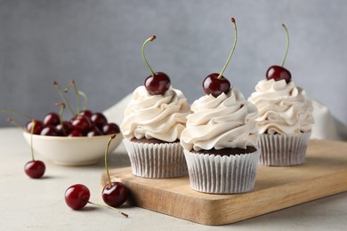 Photo of Delicious cupcakes with cream and cherries on light textured table