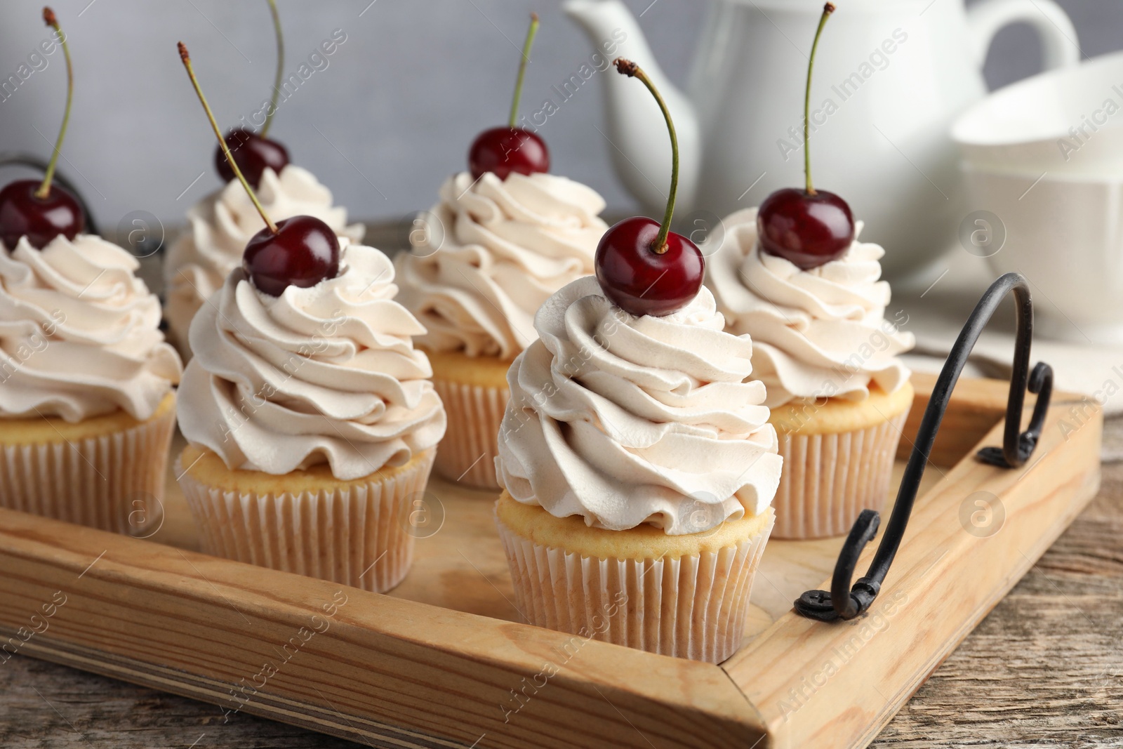 Photo of Delicious cupcakes with cream and cherries on wooden table, closeup