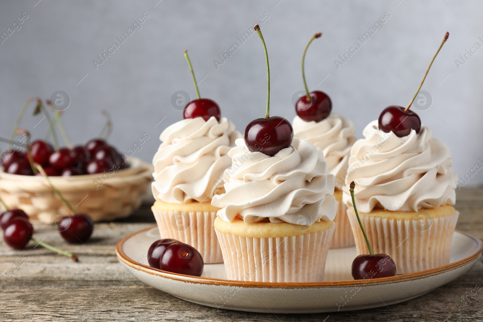 Photo of Delicious cupcakes with cream and cherries on wooden table, closeup