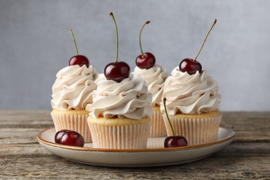 Photo of Delicious cupcakes with cream and cherries on wooden table, closeup