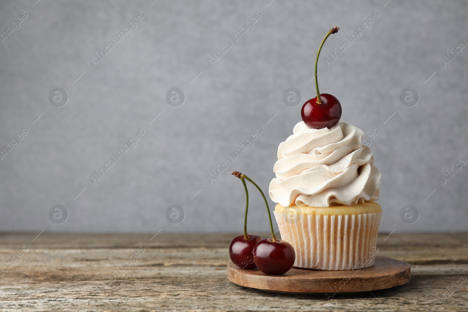 Photo of Delicious cupcake with cream and cherries on wooden table, space for text