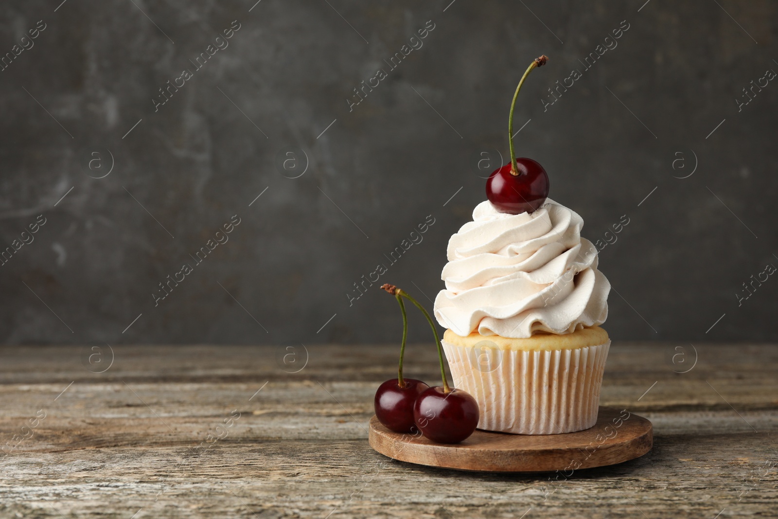 Photo of Delicious cupcake with cream and cherries on wooden table, space for text