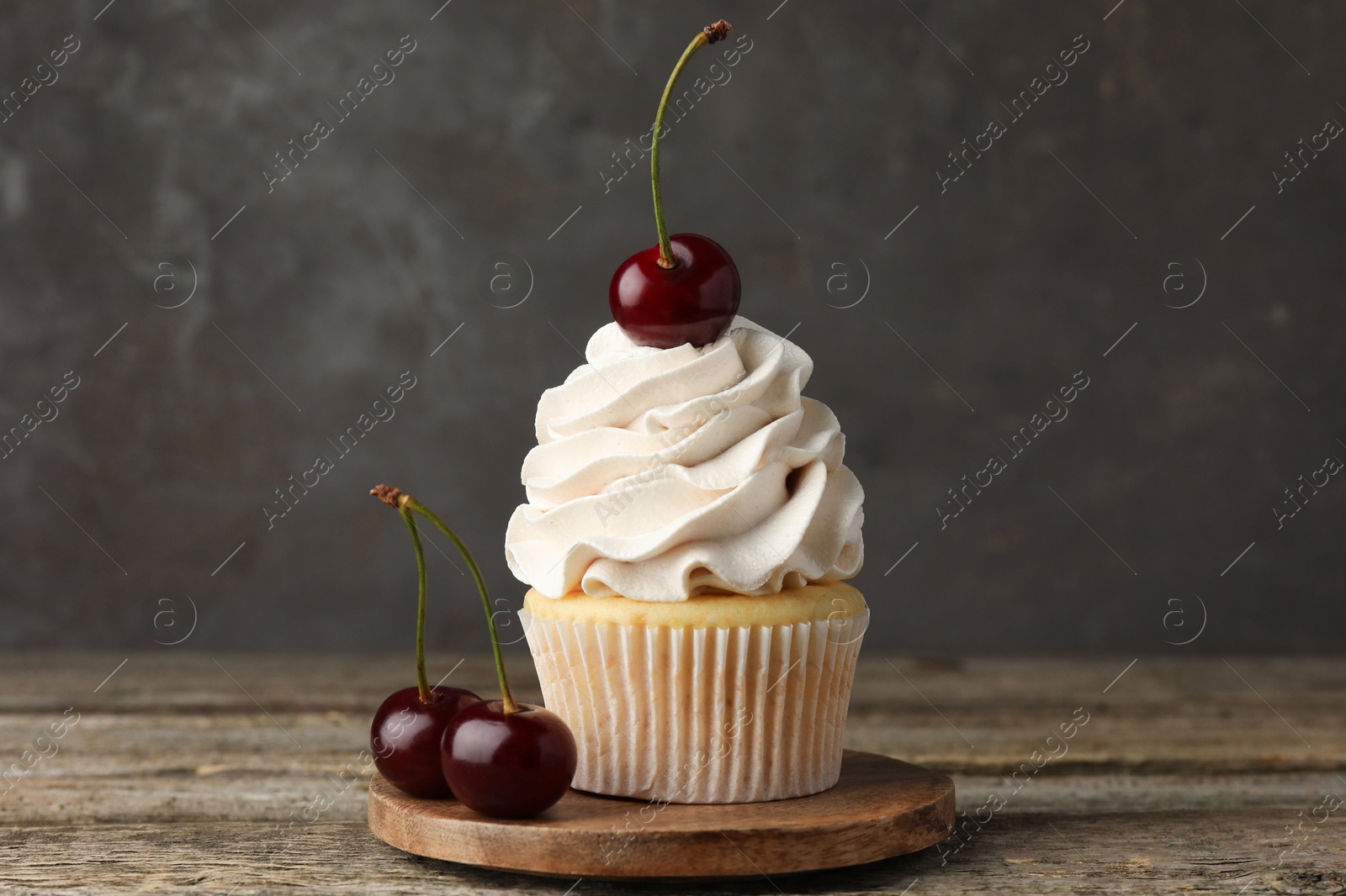 Photo of Delicious cupcake with cream and cherries on wooden table, closeup