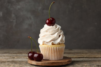 Photo of Delicious cupcake with cream and cherries on wooden table, closeup