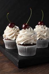 Photo of Delicious cupcakes with cream and cherries on wooden table, closeup