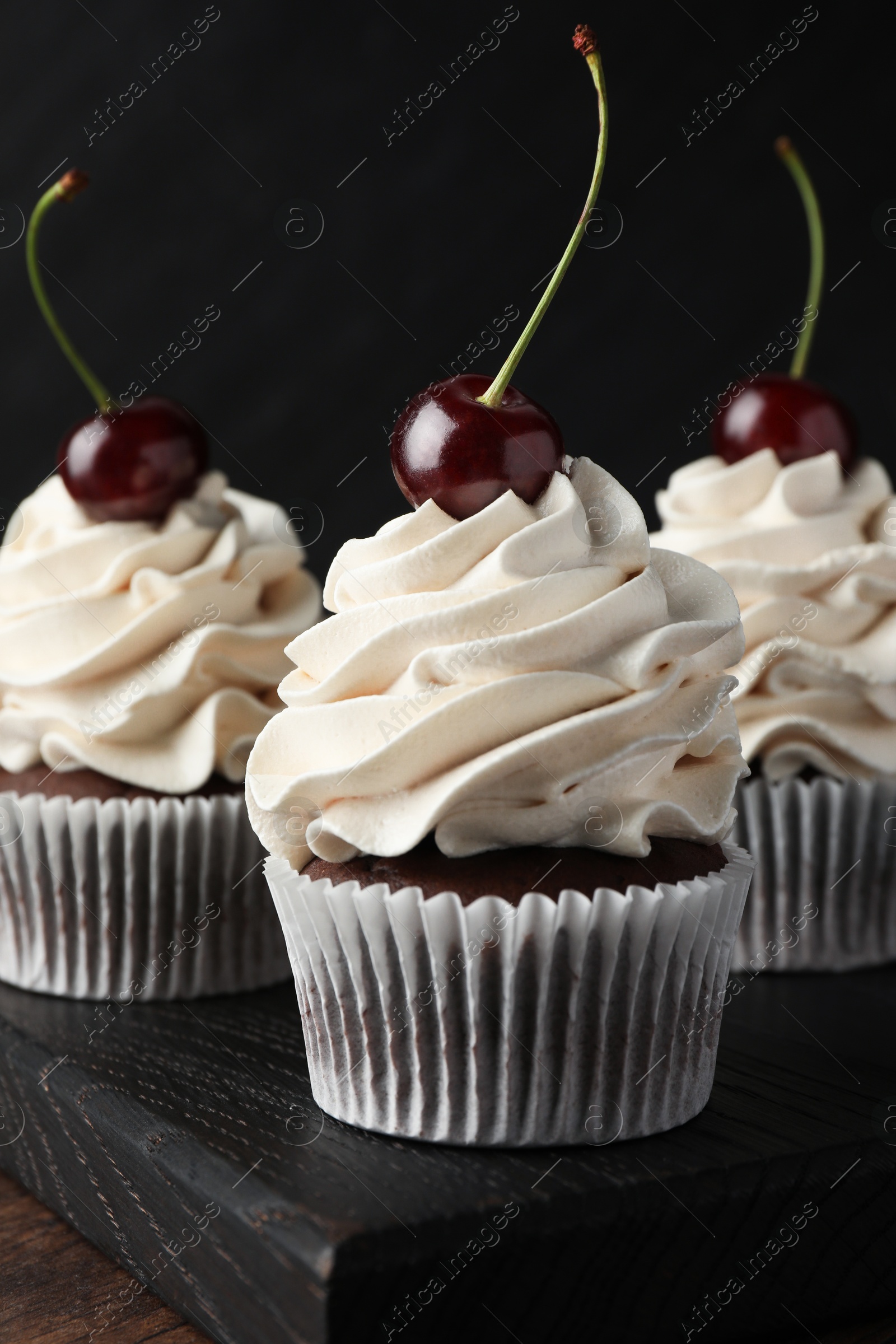 Photo of Delicious cupcakes with cream and cherries on wooden table, closeup