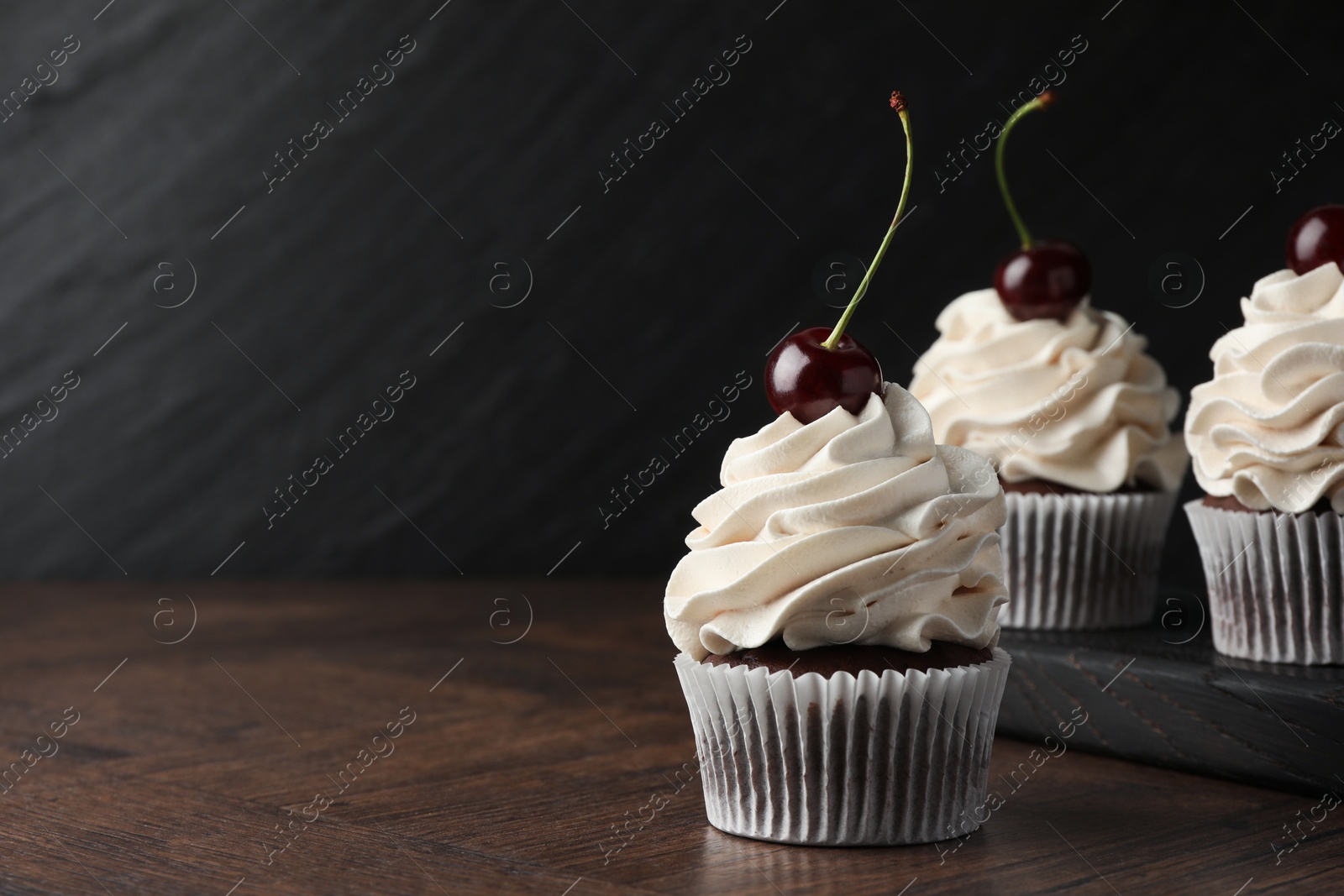 Photo of Delicious cupcakes with cream and cherries on wooden table, space for text