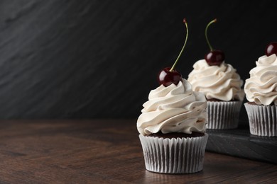 Delicious cupcakes with cream and cherries on wooden table, space for text