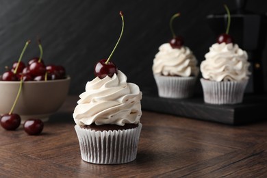 Photo of Delicious cupcakes with cream and cherries on wooden table, closeup