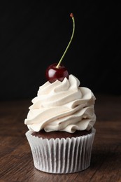 Delicious cupcake with cream and cherry on wooden table, closeup