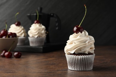 Delicious cupcake with cream and cherry on wooden table, closeup. Space for text