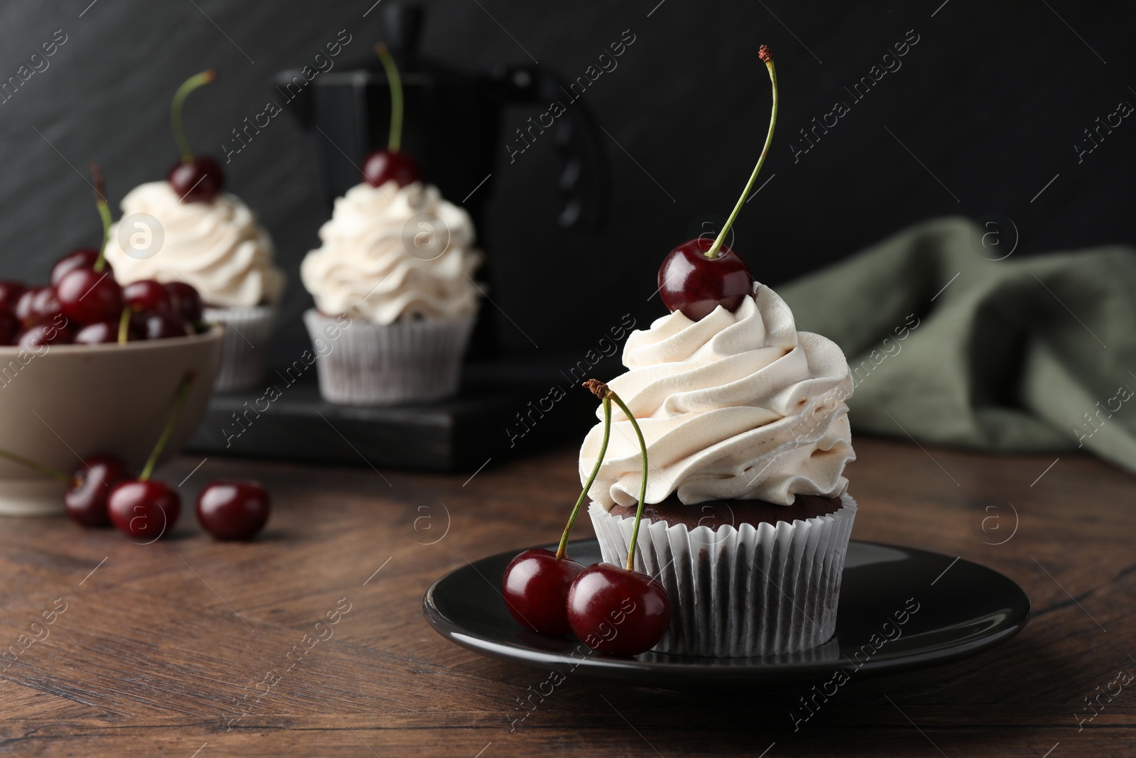 Photo of Delicious cupcakes with cream and cherries on wooden table, closeup