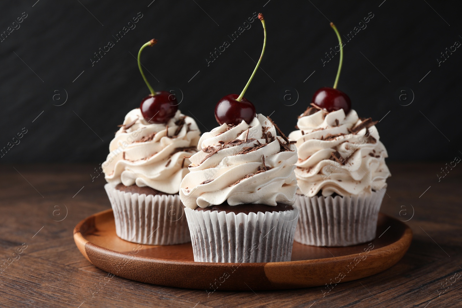 Photo of Delicious cupcakes with cream and cherries on wooden table, closeup