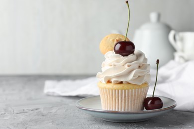 Photo of Delicious cupcake with cherries and cookie on grey textured table, closeup. Space for text