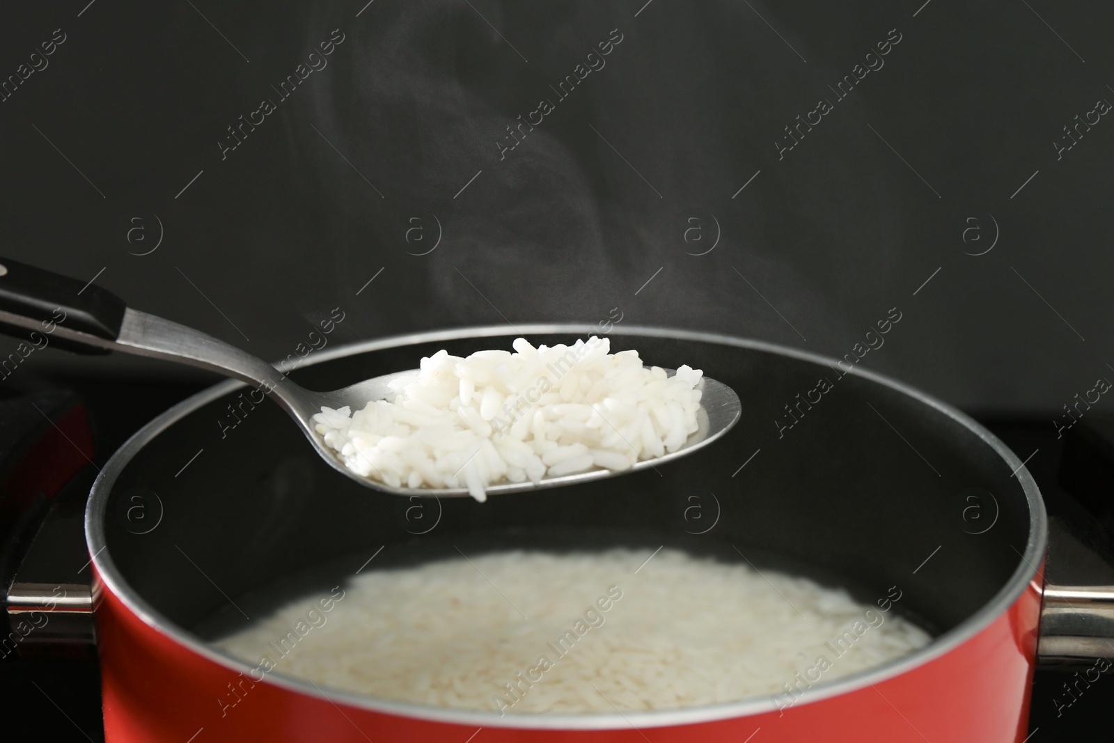 Photo of Taking boiled rice from pot with spoon on black background, closeup