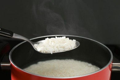 Taking boiled rice from pot with spoon on black background, closeup