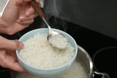 Photo of Woman taking boiled rice from pot into bowl, closeup