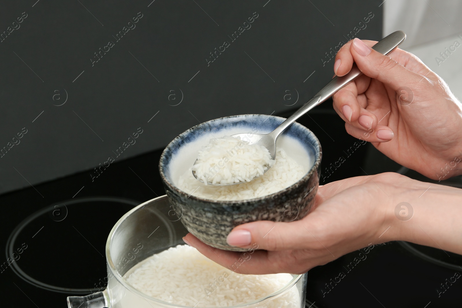 Photo of Woman taking boiled rice from pot into bowl, closeup