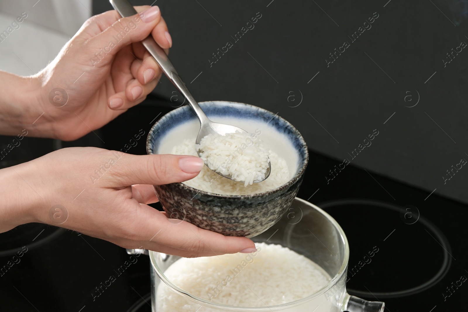 Photo of Woman taking boiled rice from pot into bowl, closeup