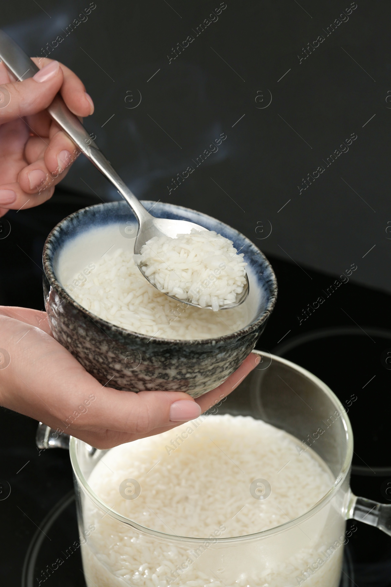 Photo of Woman taking boiled rice from pot into bowl, closeup