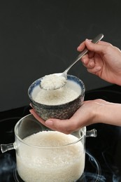 Photo of Woman taking boiled rice from pot into bowl, closeup