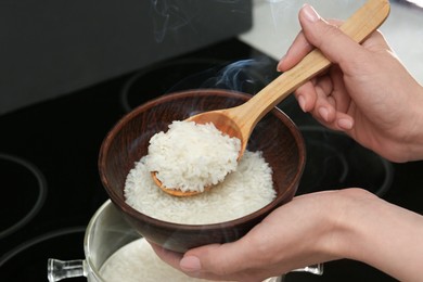 Photo of Woman taking boiled rice from pot into bowl, closeup