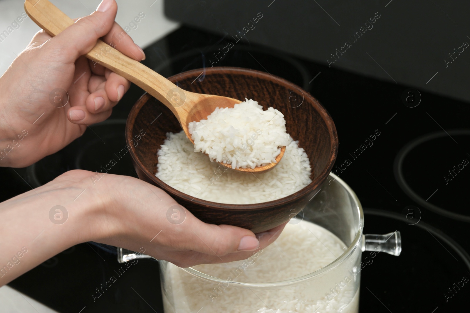 Photo of Woman taking boiled rice from pot into bowl, closeup