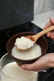 Photo of Woman taking boiled rice from pot into bowl, closeup