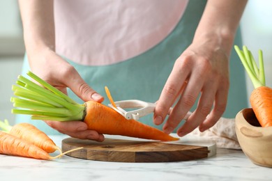 Photo of Woman peeling fresh carrot at white marble table, closeup