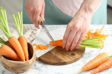 Photo of Woman cutting fresh carrot at white marble table, closeup