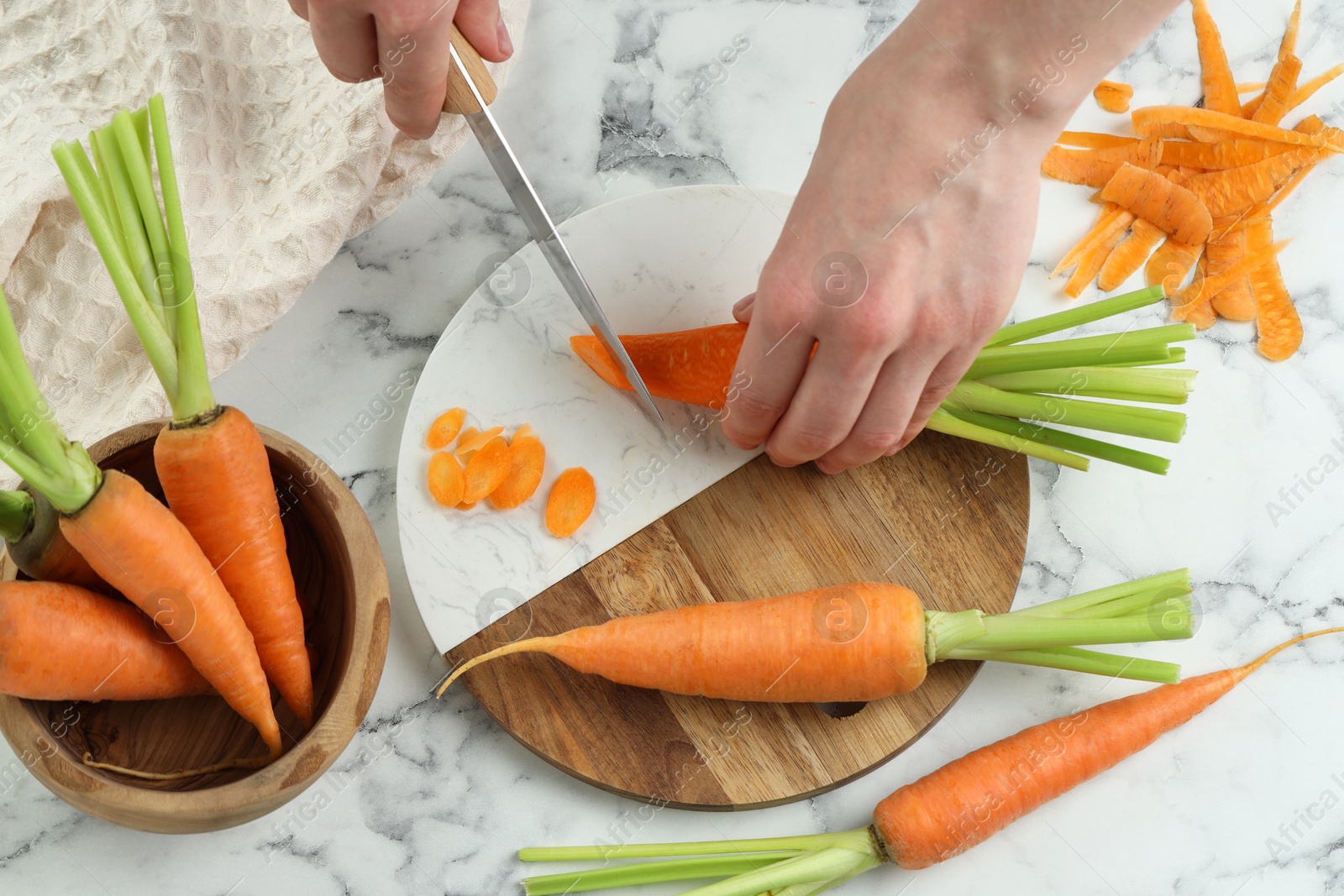 Photo of Woman cutting fresh carrot at white marble table, top view