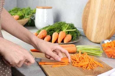 Photo of Woman cutting fresh carrot at gray textured table, closeup