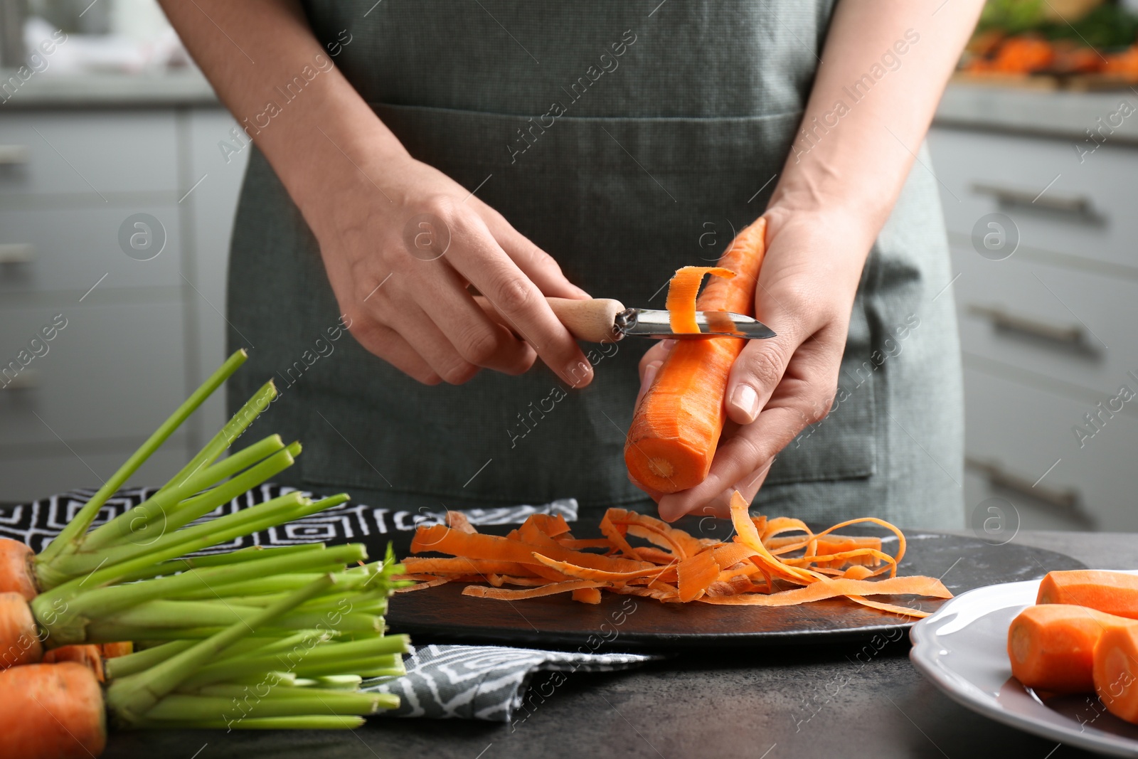 Photo of Woman peeling fresh carrot at dark gray table in kitchen, closeup