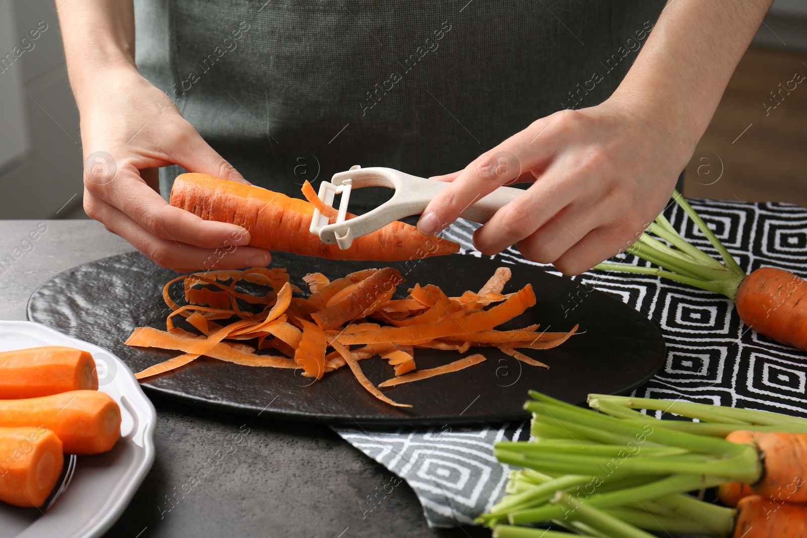 Photo of Woman peeling fresh carrot at dark gray table, closeup