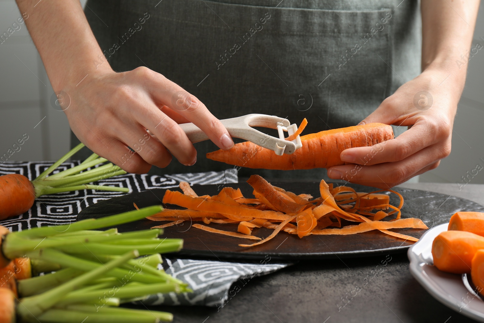 Photo of Woman peeling fresh carrot at dark gray table, closeup