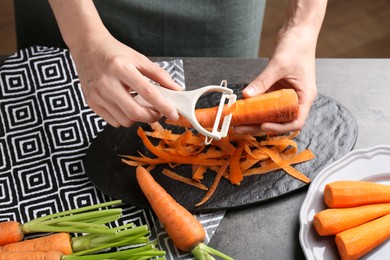 Photo of Woman peeling fresh carrot at dark gray table, closeup