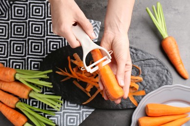 Photo of Woman peeling fresh carrot at dark gray table, top view