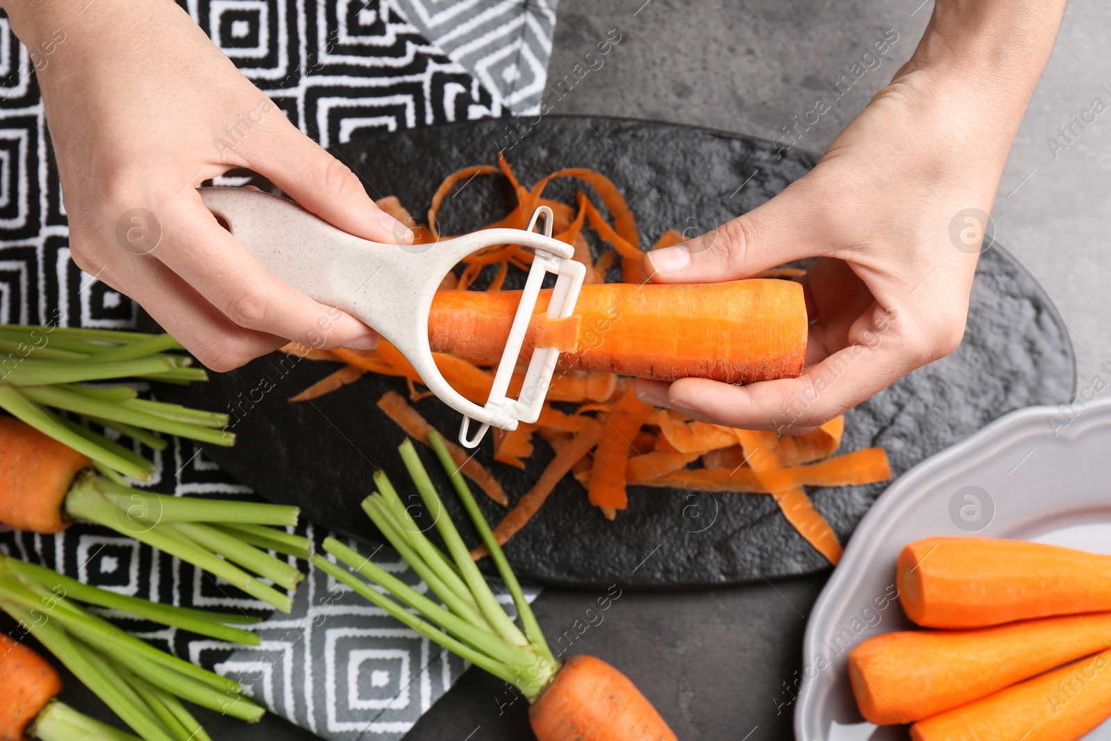 Photo of Woman peeling fresh carrot at dark gray table, top view