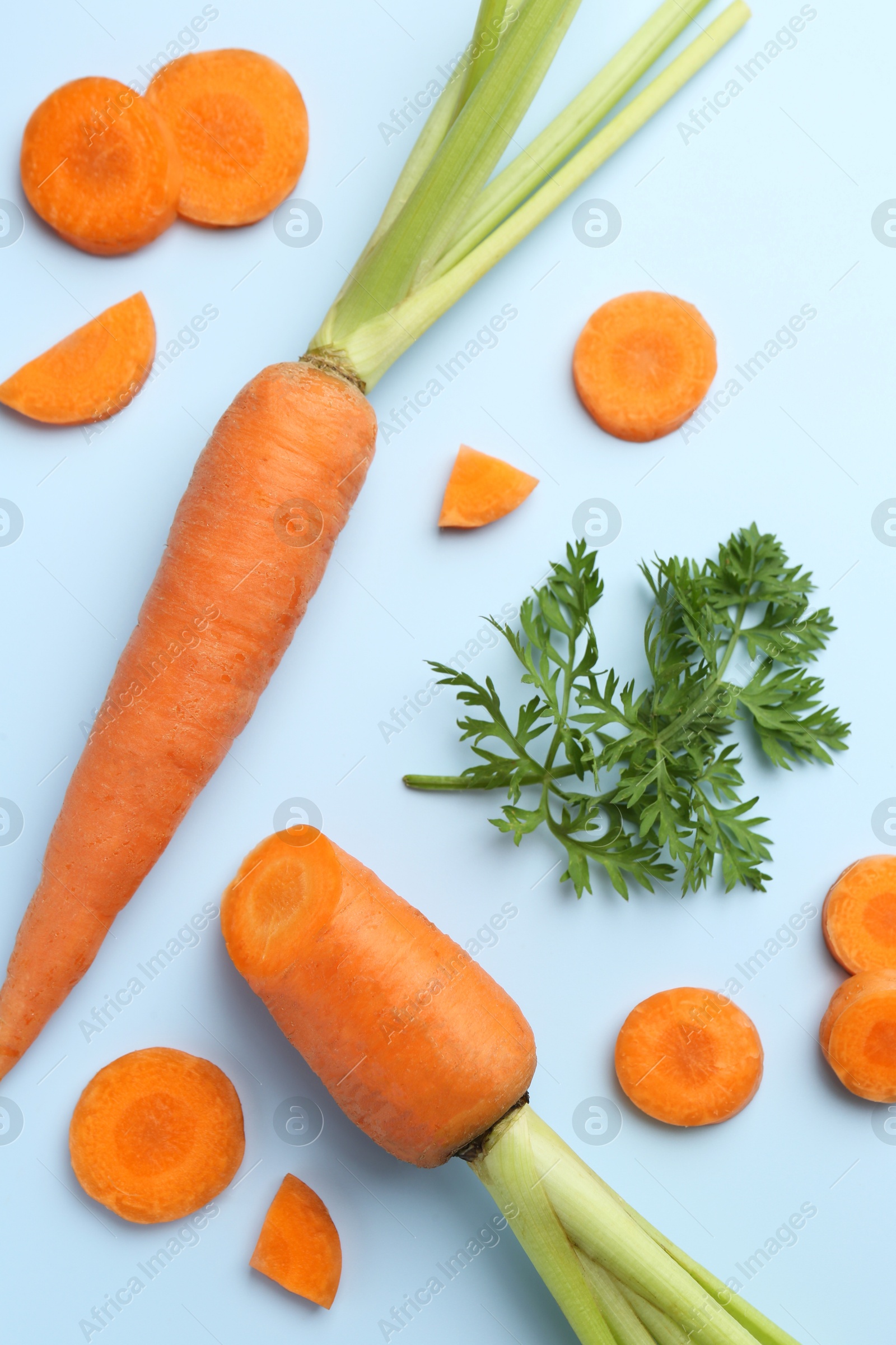 Photo of Whole and cut fresh carrots with green leaf on light background, flat lay