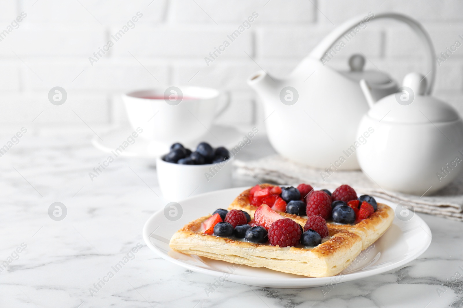 Photo of Tasty puff pastries with berries and tea on white marble table, space for text