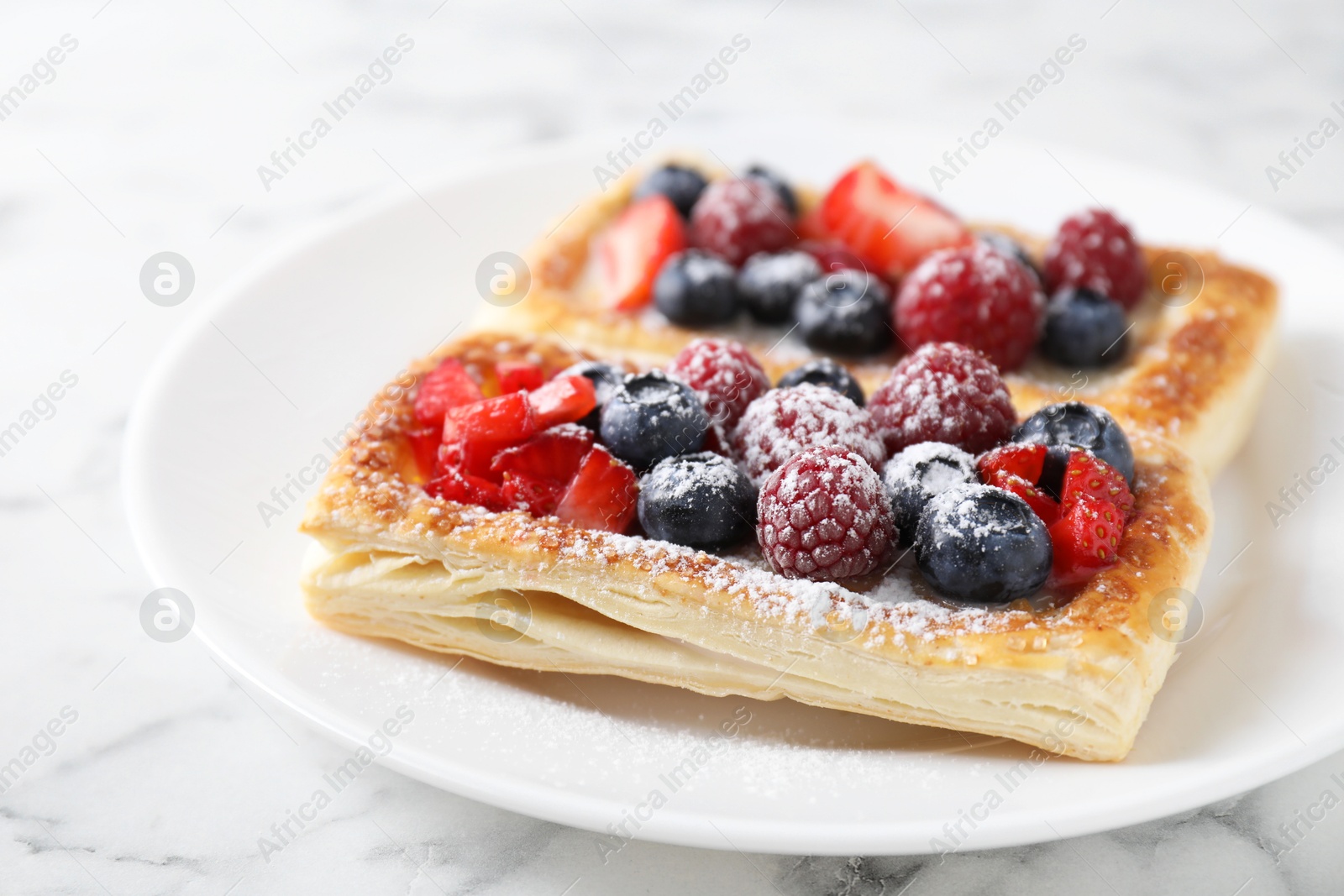 Photo of Tasty puff pastries with berries on white marble table, closeup