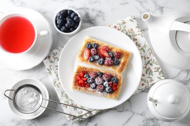 Photo of Tasty puff pastries with berries and tea on white marble table, flat lay