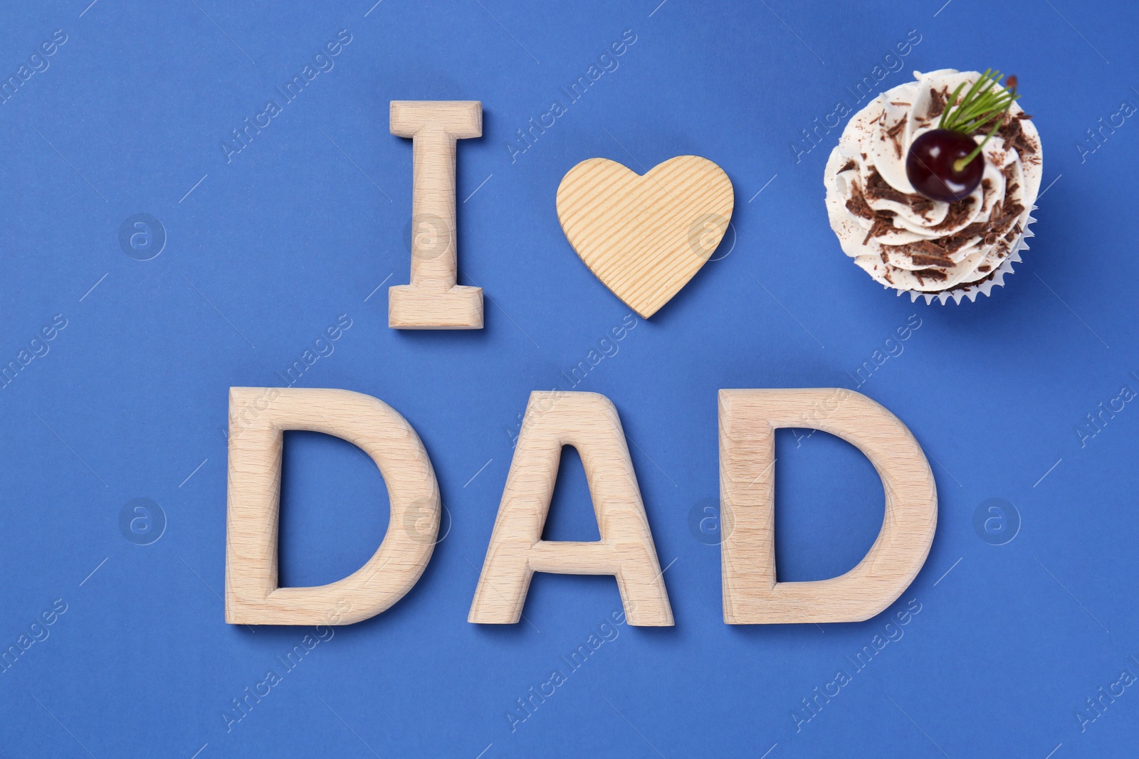 Photo of Happy Father's Day. Phrase I love Dad made with wooden letters, decorative heart and cupcake on blue background, flat lay