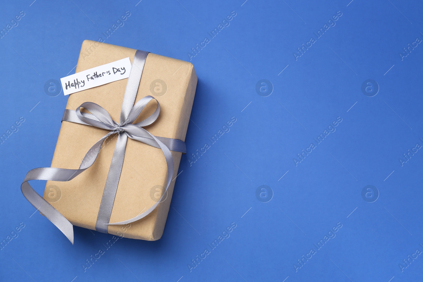 Photo of Gift box and note with phrase Happy Father's Day on blue background, top view. Space for text