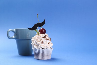 Photo of Happy Father's Day. Cupcake with mustache topper and cup on blue background. Space for text