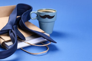 Photo of Happy Father's Day. Paper bag with book, tie and cup of coffee on blue background, closeup. Space for text