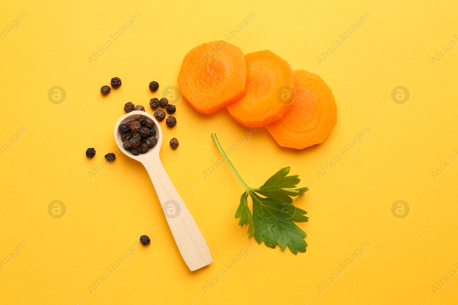 Photo of Slices of fresh ripe carrot, spices and spoon on yellow background, flat lay