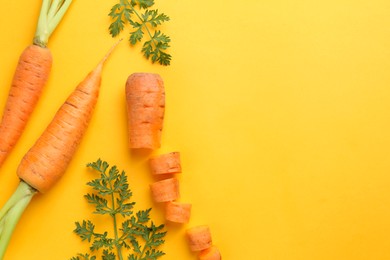 Photo of Whole and cut fresh carrots with green leaves on yellow background, flat lay. Space for text