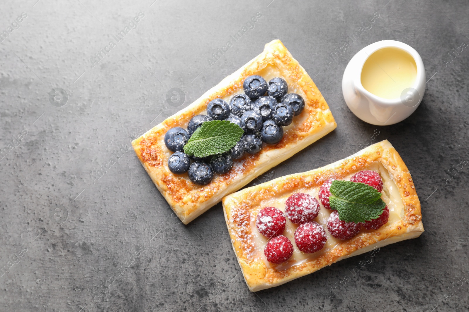 Photo of Tasty puff pastries with berries and powdered sugar on grey table, flat lay. Space for text